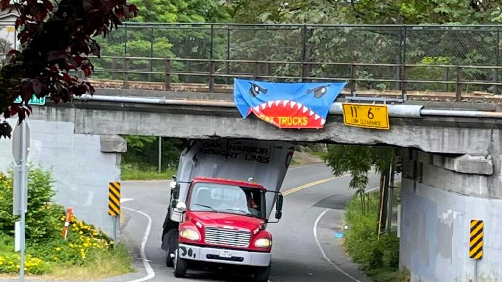 An image of a truck stucked under a pedestrian bridge with a banner overhead that declares "I eat trucks"