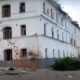 Sviatohirsk Cave Monastery in Ukraine with the larger white out buildings just past the main gate. The historic three story building on the left with windows that are rounded on the top, is pocked and scarred from artillery shells that landed within the historic compound