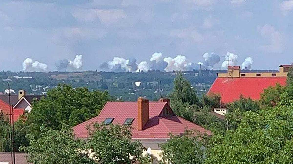 Some rises on the horizon as the 1st Army Corps shells Ukrainian positions in Avdiivka. The red roofs of Donetsk are in the foreground with the town of Avdiivka out of sight over a ridge, it is midday in summer with hazy clouds in the sky and lush trees