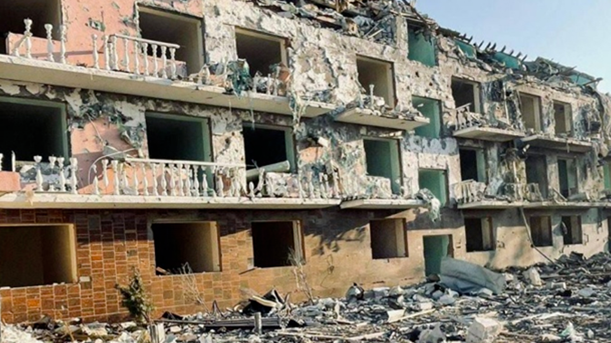 A picture of a hotel that was 4 stories tall, the 4th floor is destroyed and the other floors are severely damaged from a Russian cruise missile strike. All the windows are blown out and sections of the building are missing, the roof is collapsed