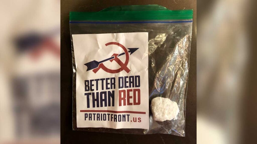 Members of Patriot Front left flyers in Kirkland driveways in January 2019

The picture shows a small Ziploc style plastic bag with a piece of white marble stone inside. To the left is a red white and blue flyer that says the Cold War slogan, better dead than red with the URL for the hate group