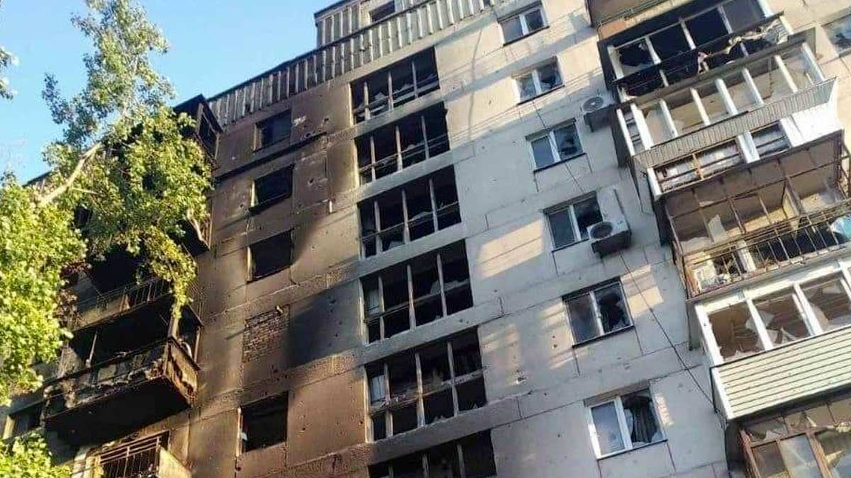 A building in an unknown location is heavily damaged after an artillery strike that caused a fire. All the windows are broken out and the façade is scorched