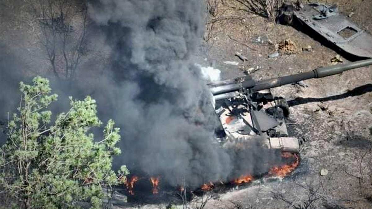 A Russian self-propelled gun, a tracked vehicle, is in flames with black smoke rising after being hit by Ukrainian artillery fire. The picture is taken in daylight and there are no buildings or roads visiible