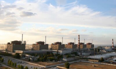 A photo of the Zaporizhzhia Nuclear Power Plant before the war in morning light, looking at the six reactor buildings. The Dnipro River can be seen in the background, the sky has high clouds