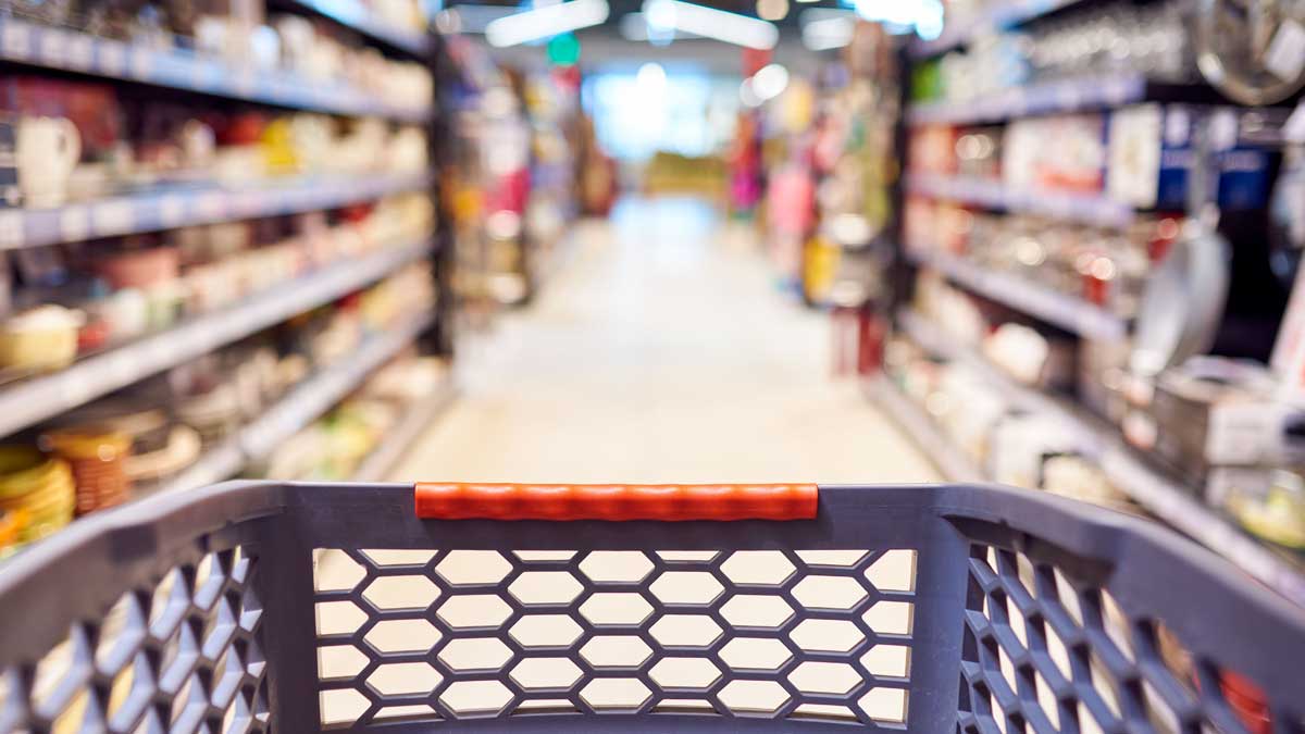 An out of focus grocery store with a shopping cart in the foreground